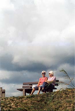 women on a bench with dramatic clounds in background
